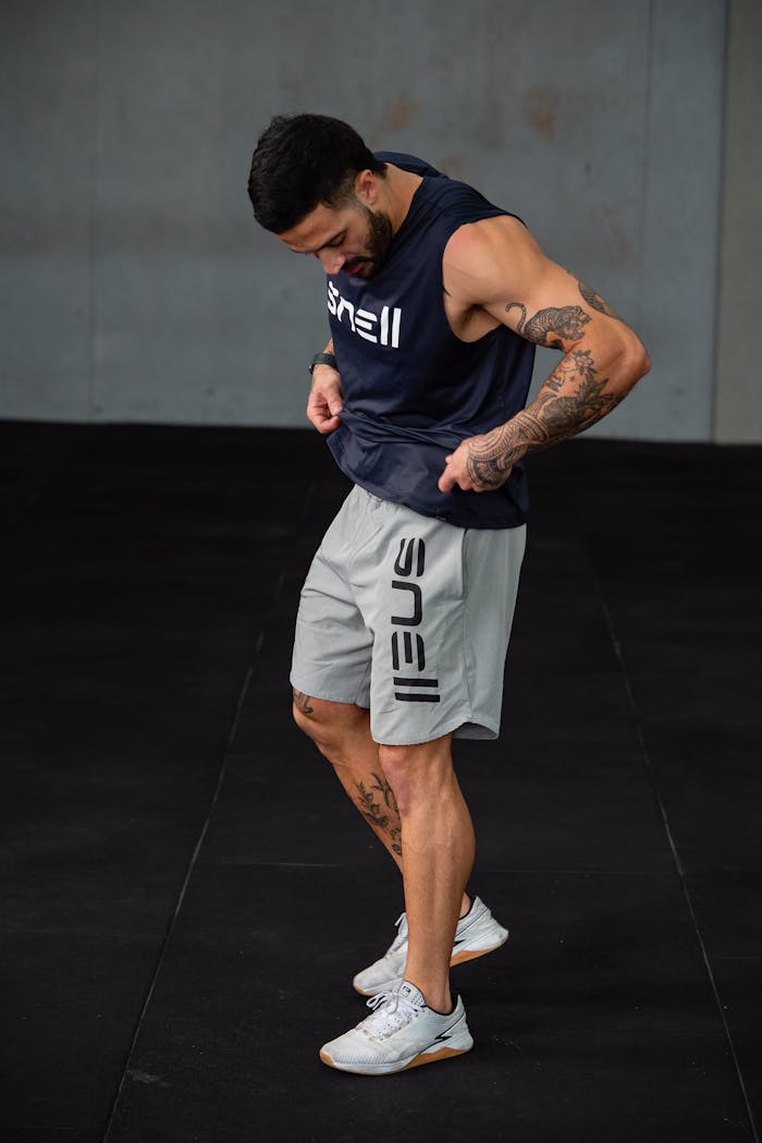 Athletic man standing in a gym, showcasing his muscular build and tattoos. Ideal for fitness and sports themes.