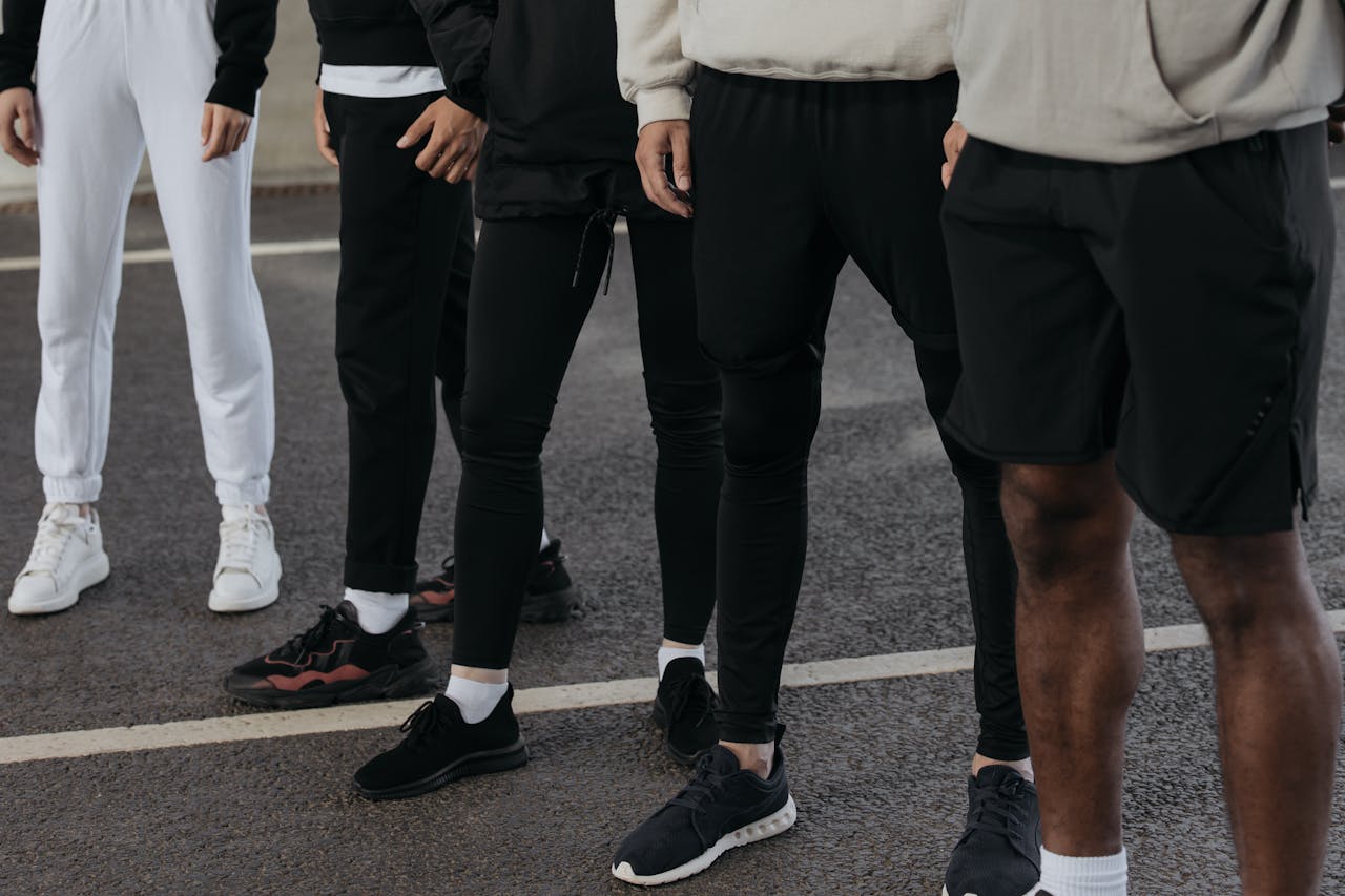 A diverse group of people in activewear standing on an outdoor pavement wearing sneakers.